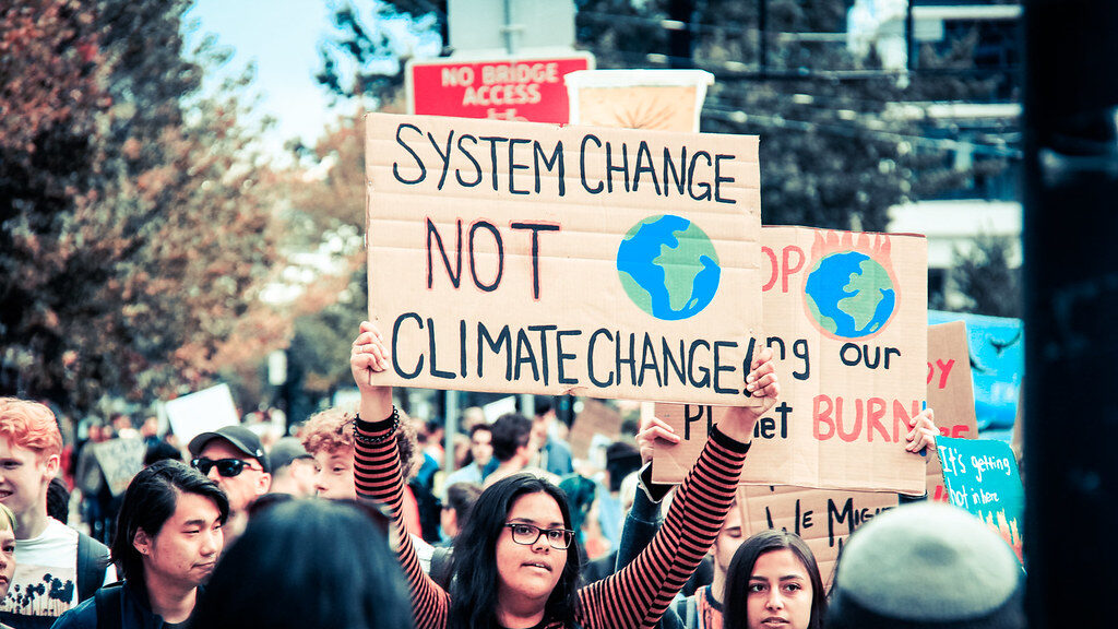 "System change, not climate change" by <a href="https://www.flickr.com/photos/doucy/" target="_blank" rel="noopener">Chris Yakimov</a>  is licensed under <a href="https://creativecommons.org/licenses/by-nc/2.0/" target="_blank" rel="noopener">CC BY-NC 2.0</a>